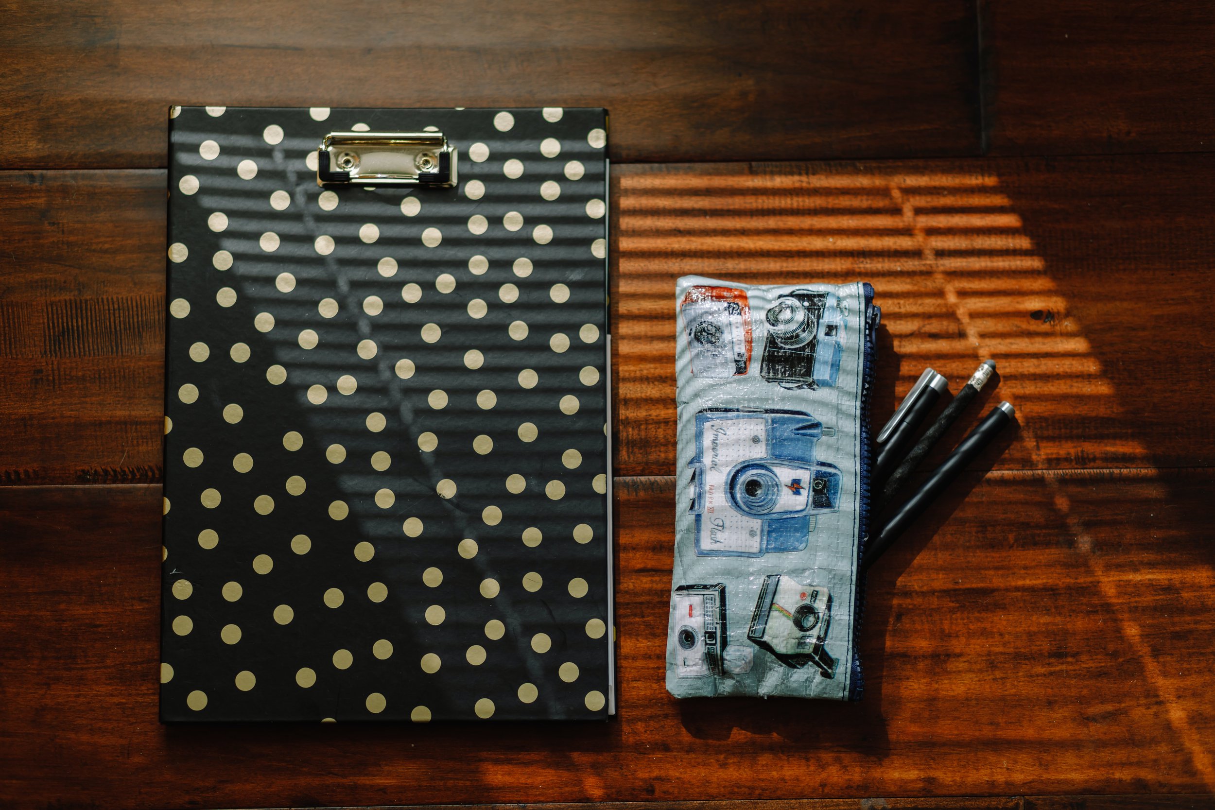 Photo of a workspace with a clipboard and pen holder with striped lights coming through the blinds