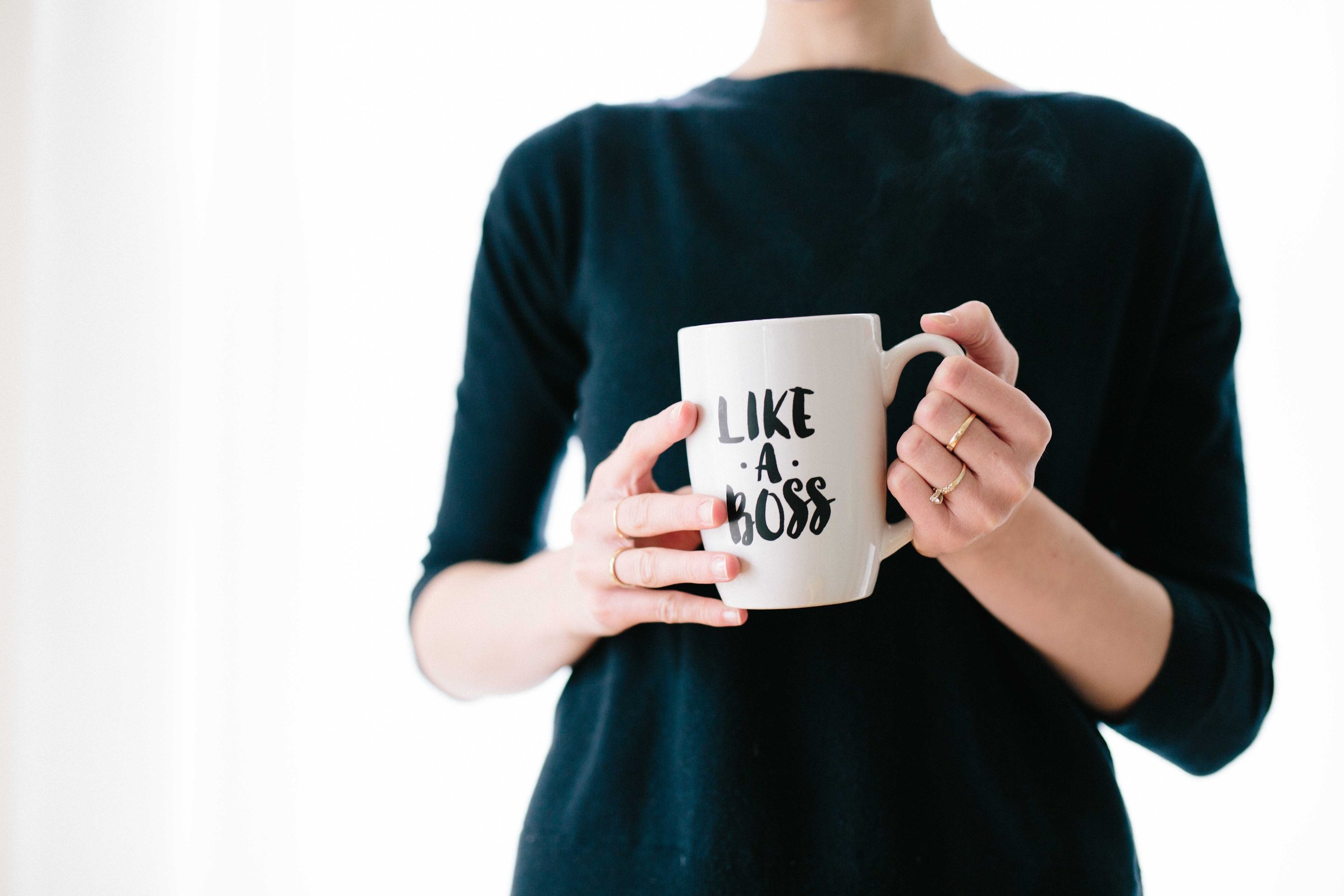 Photo of a woman with gold rings holding a mug that says LIKE A BOSS
