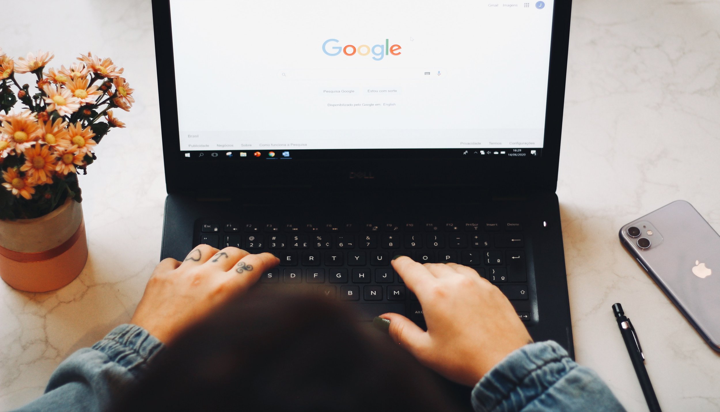 Photo of a person's hands on their laptop next to a cup of flowers