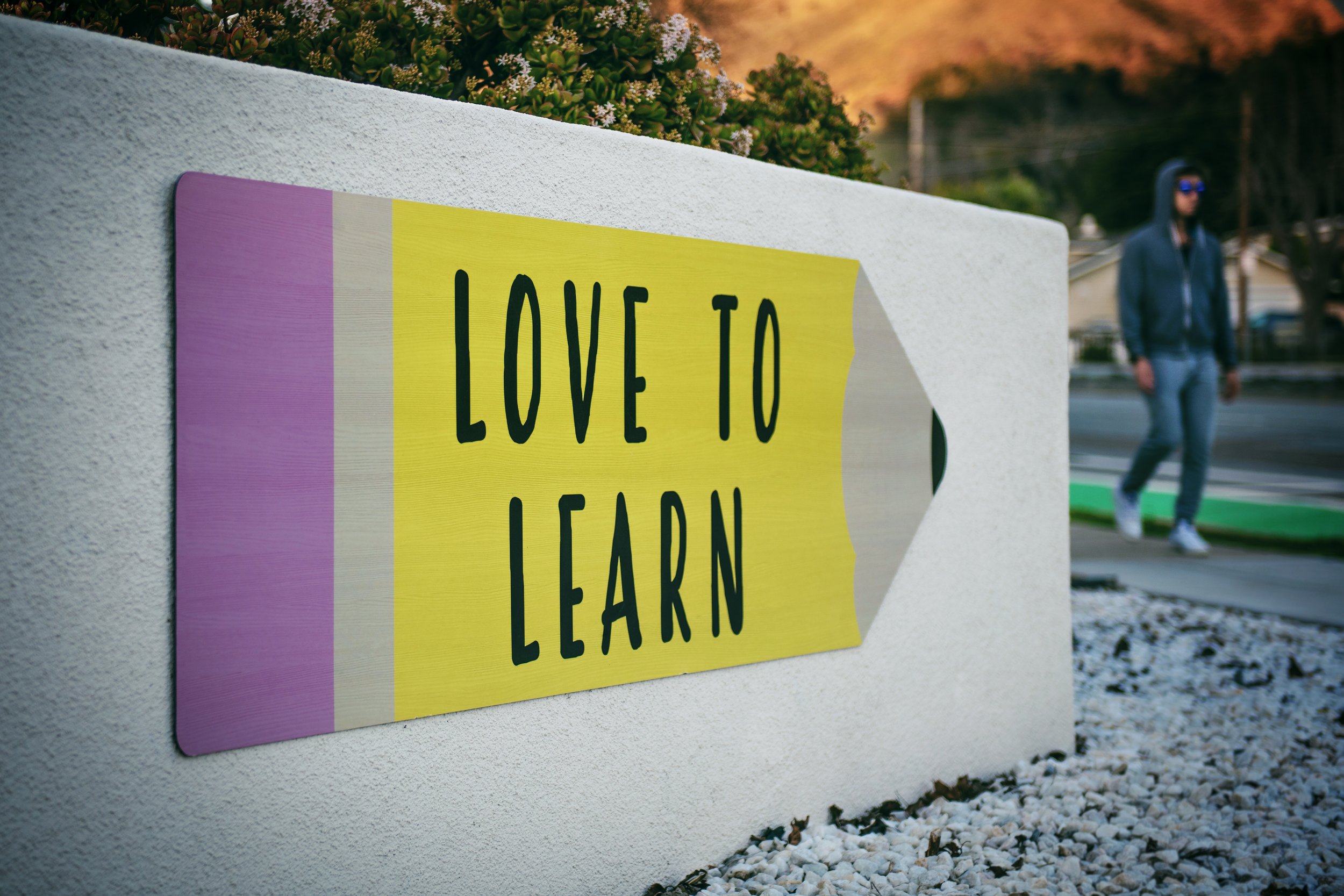 Photo of an outdoors wall with a poster of a pencil on it that says LOVE TO LEARN
