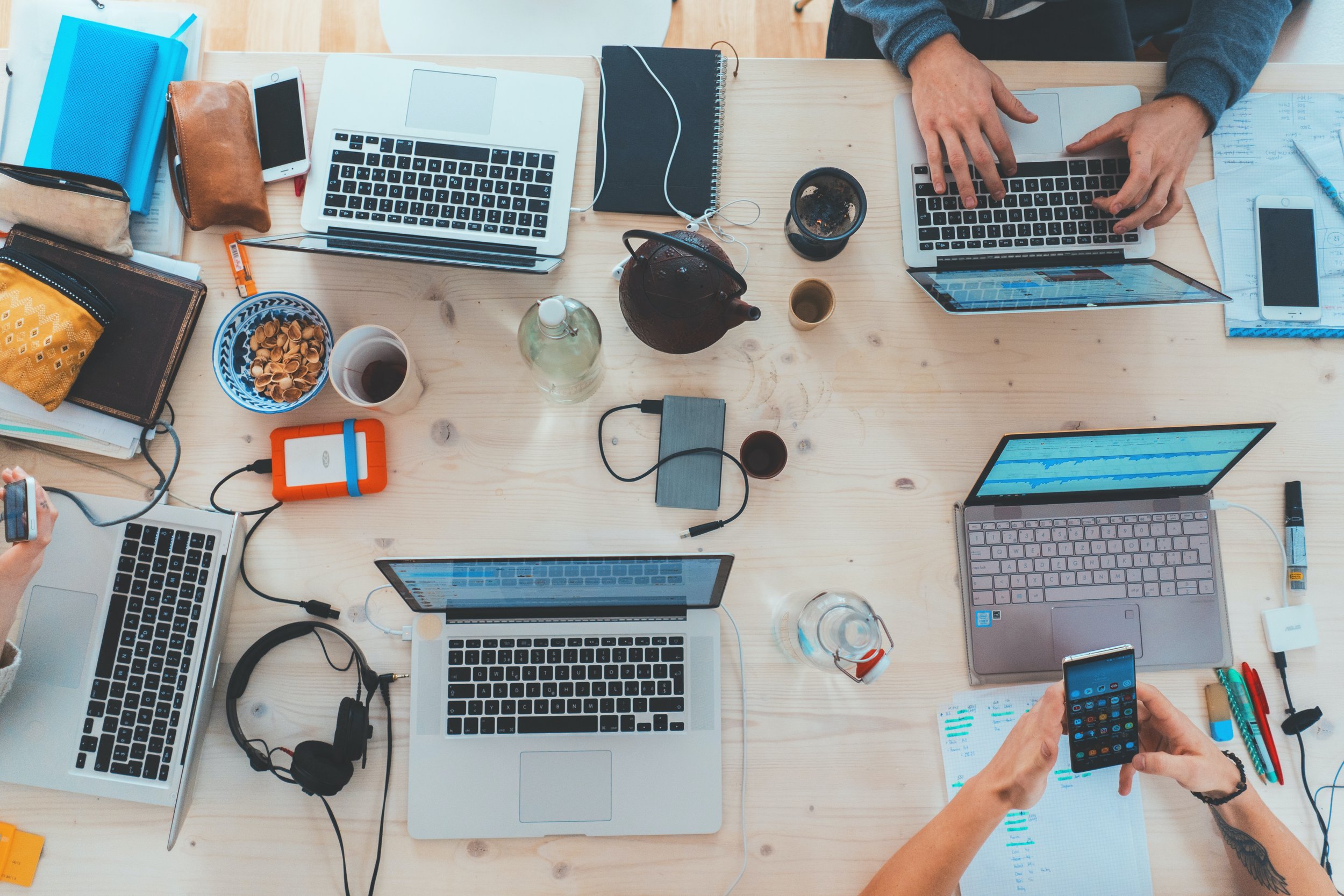Picture from above of a table covered in laptops at a coworking space with pistachios and tea