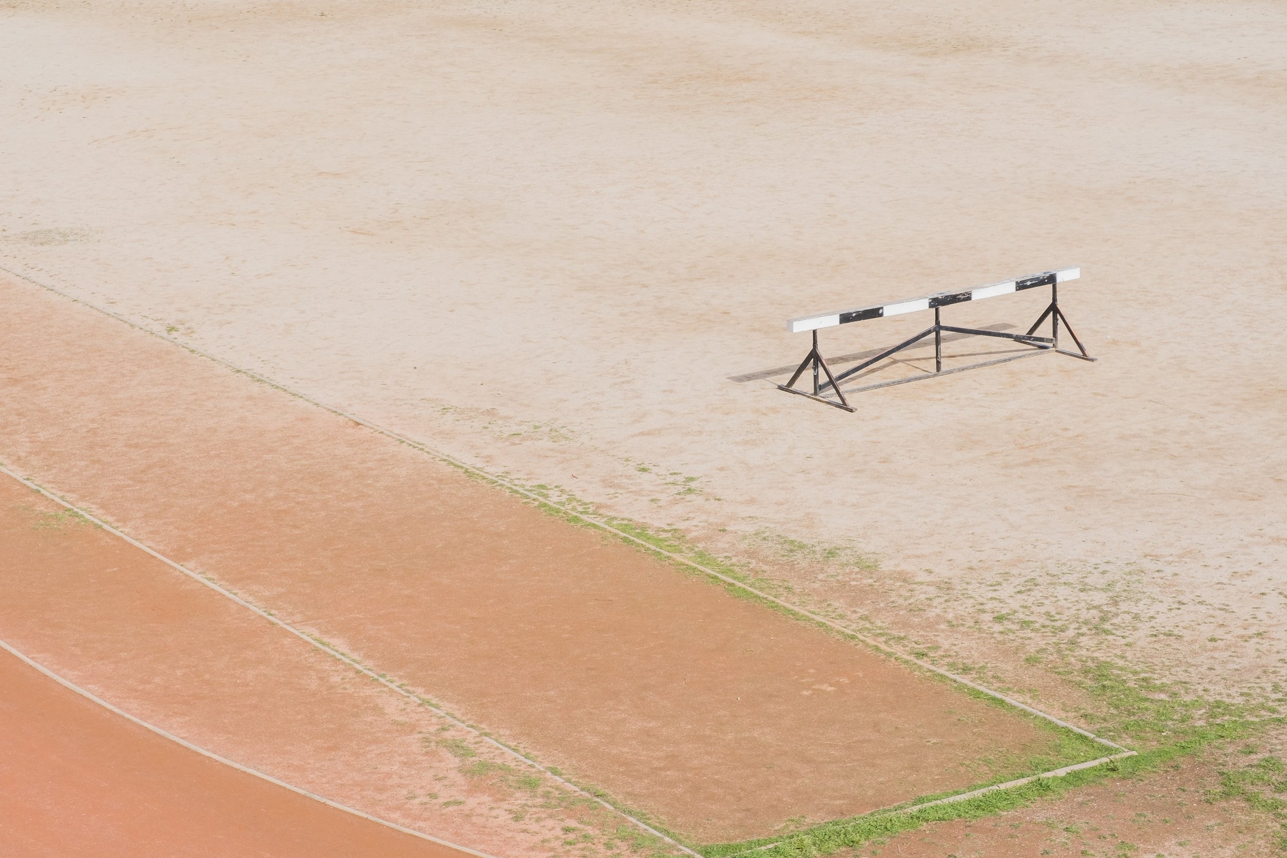 Photo of running race track outdoors with a striped hurdle sitting in the middle of the field.