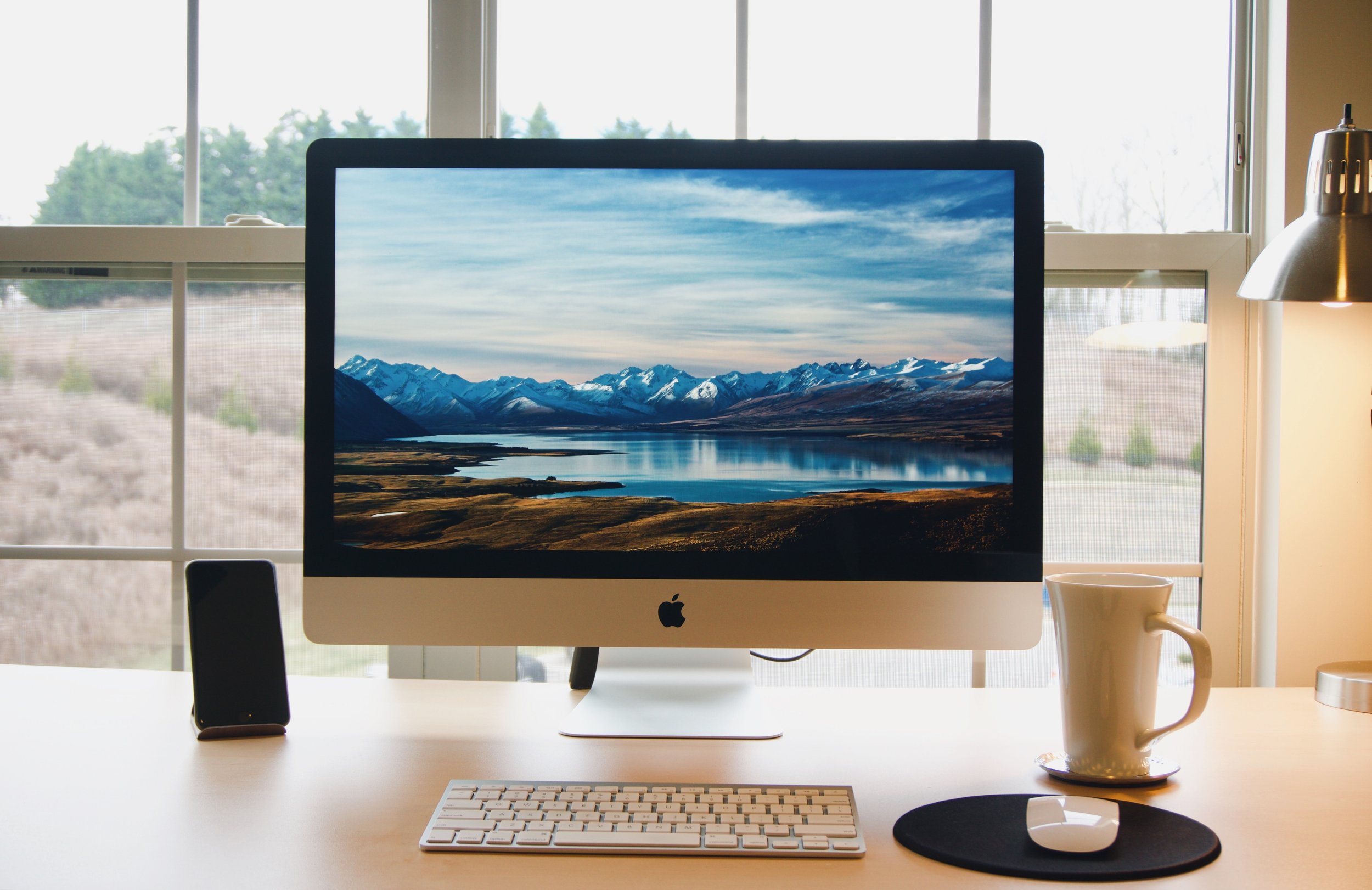 Photo of an Apple computer on a desk in a home office with a cup of coffee off to the side