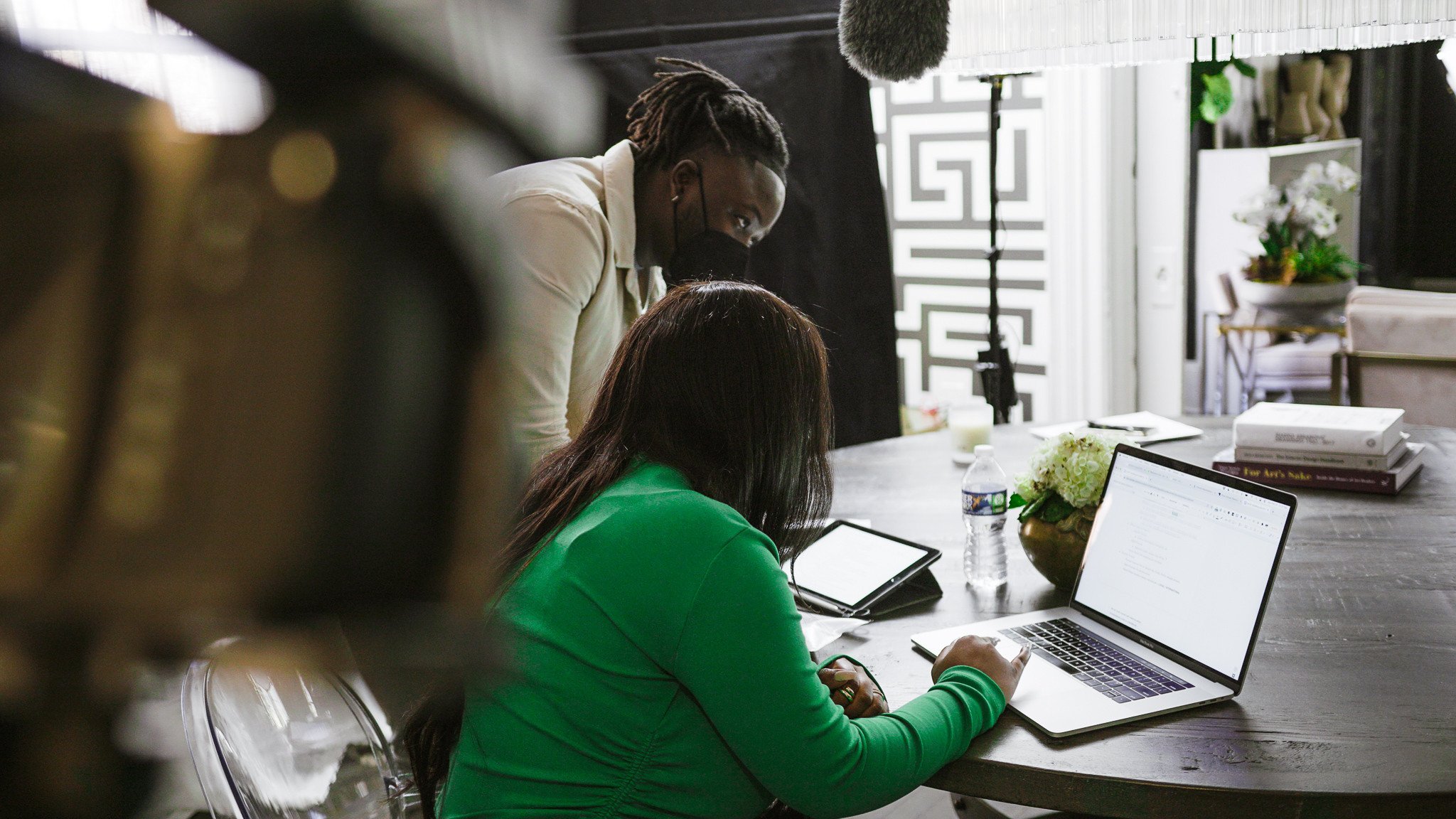 Photo of a Black man and woman in masks gathered around a laptop in a corporate office setting