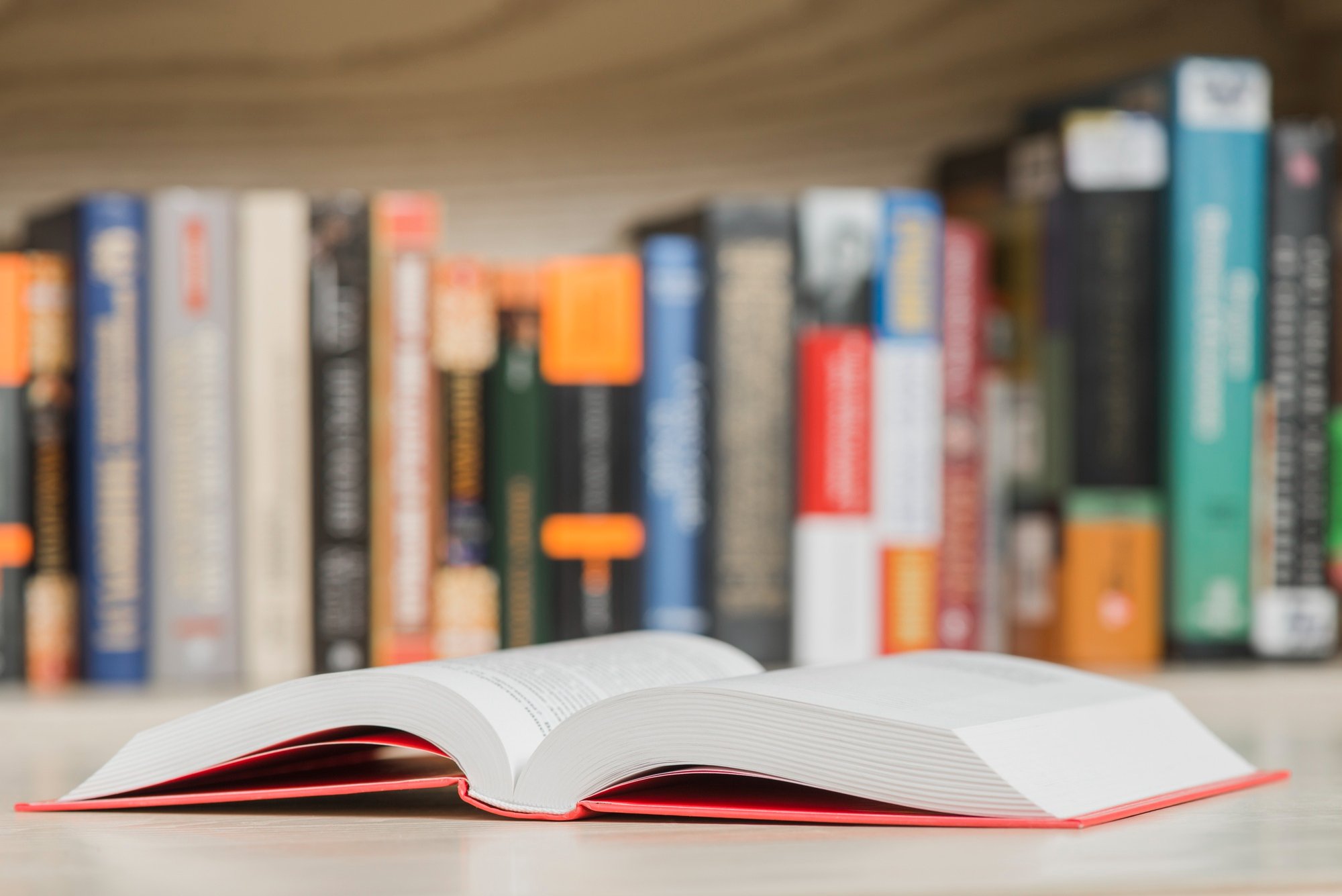 An open book sits on a table in a library with books on shelves in the background