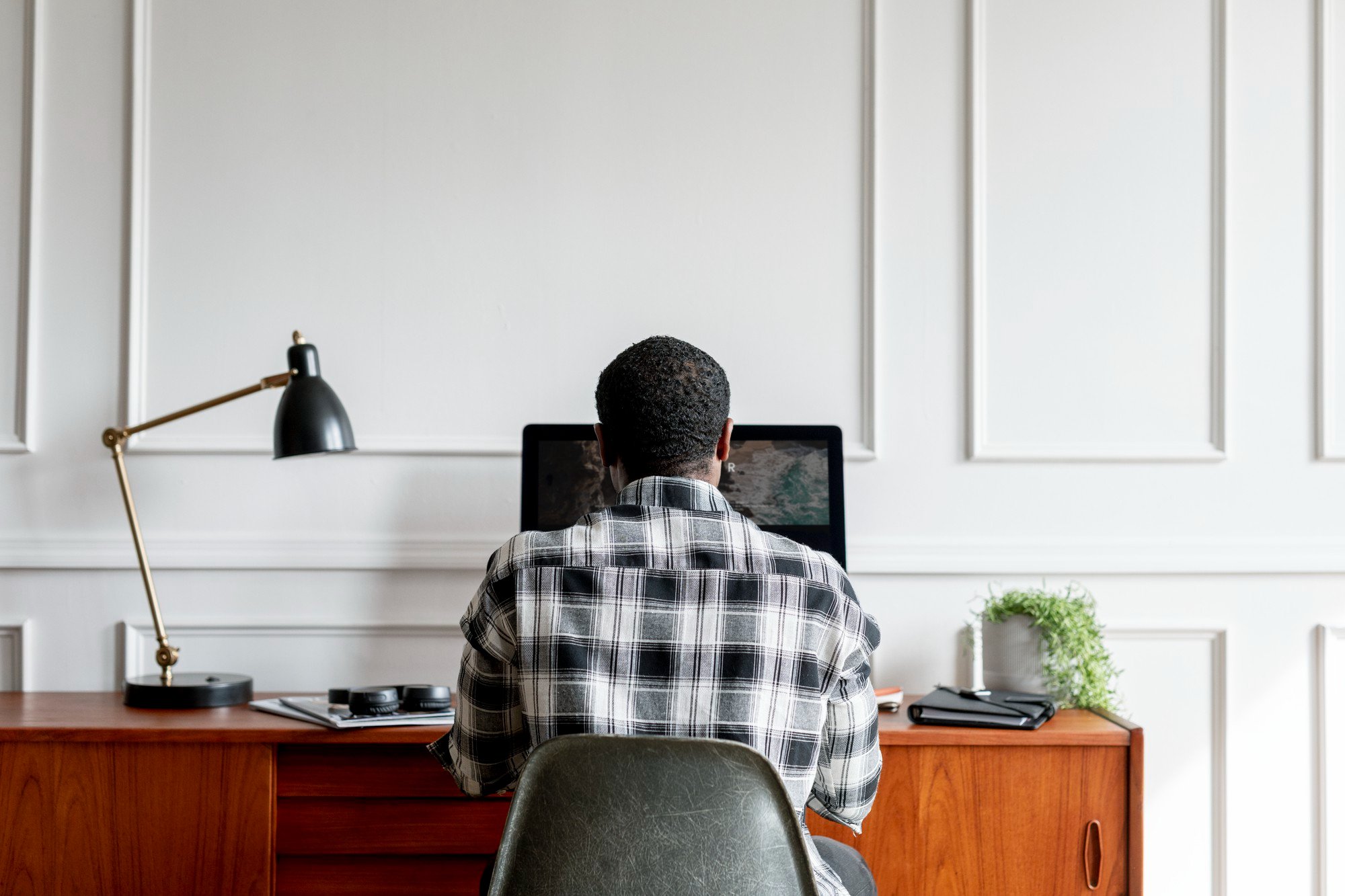 A Black man works at a desk on a computer in his home office
