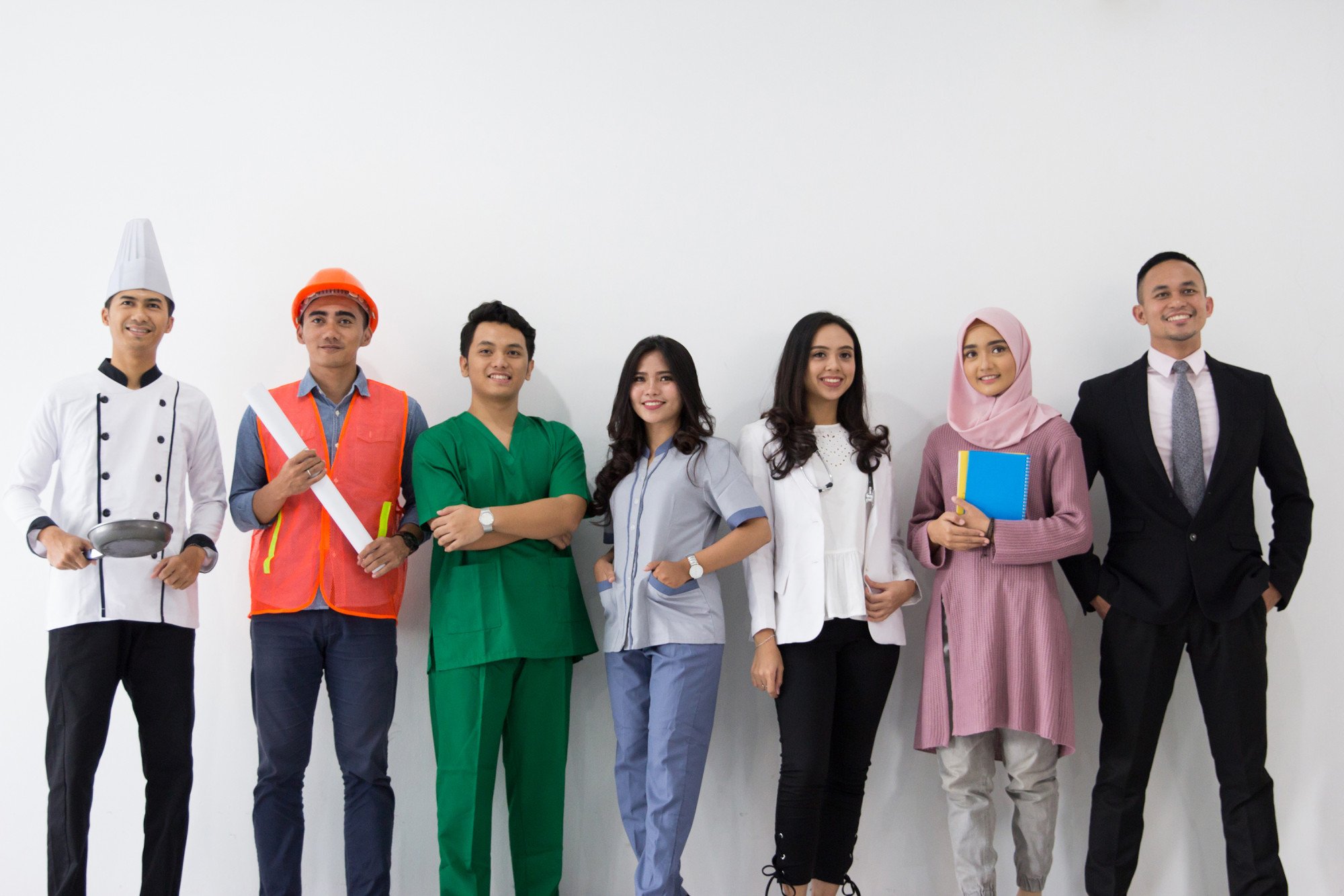 A group of Southeast Asian workers stand in a line wearing different uniforms: a chef, construction worker, doctor, businessperson, etc.