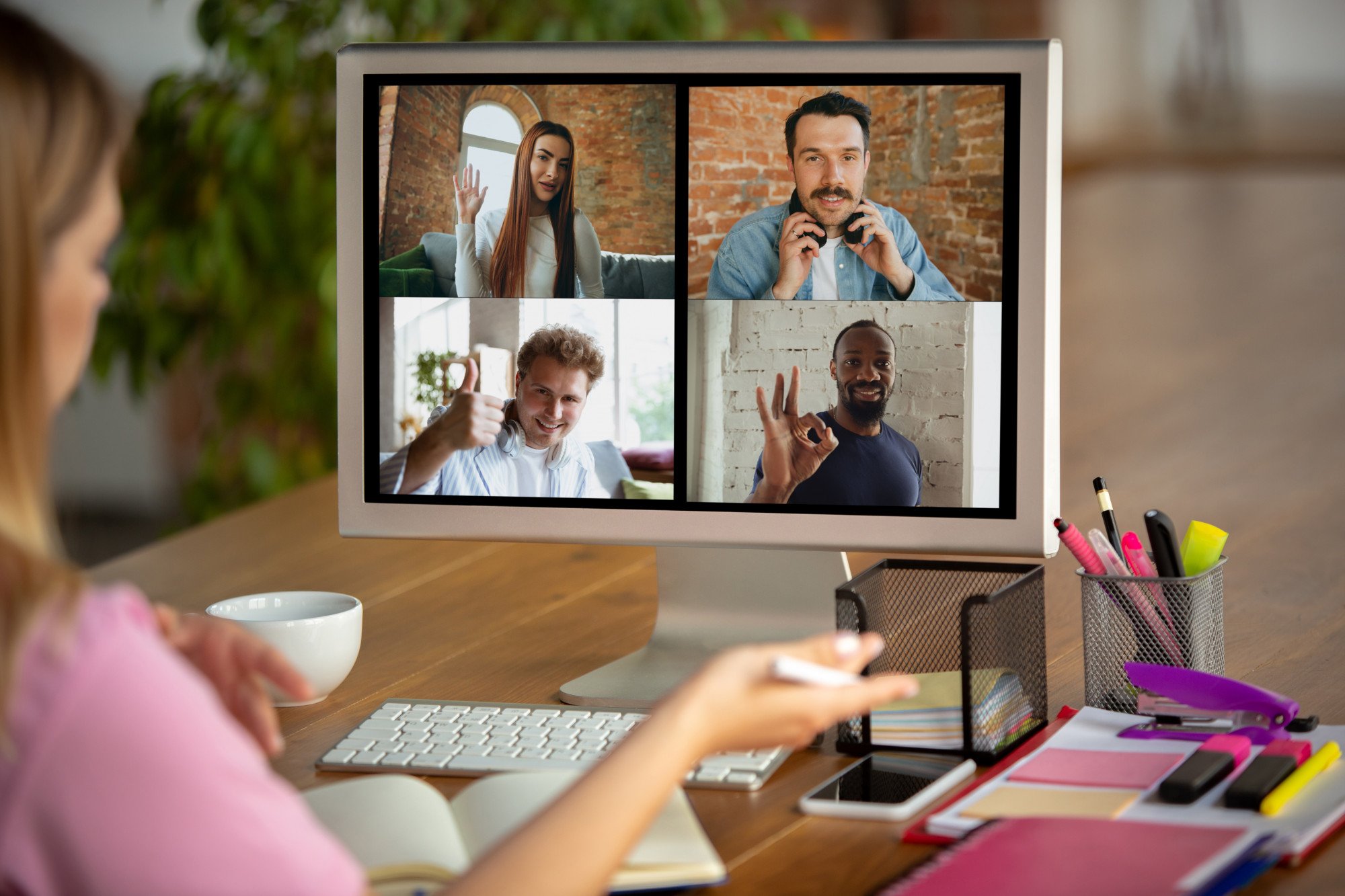 A computer monitor shows a corporate team on a conference call, and individuals give a thumbs-up at their webcams.