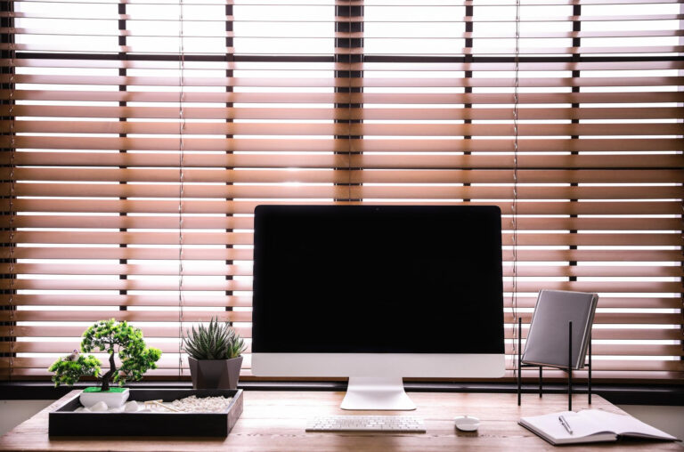 A desktop computer sits on a desk with blinds closed behind it