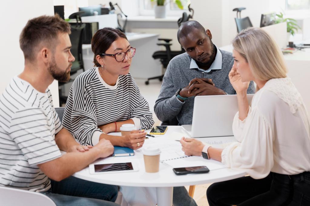 A diverse corporate team gathers in an office for a meeting and sits around a table together.