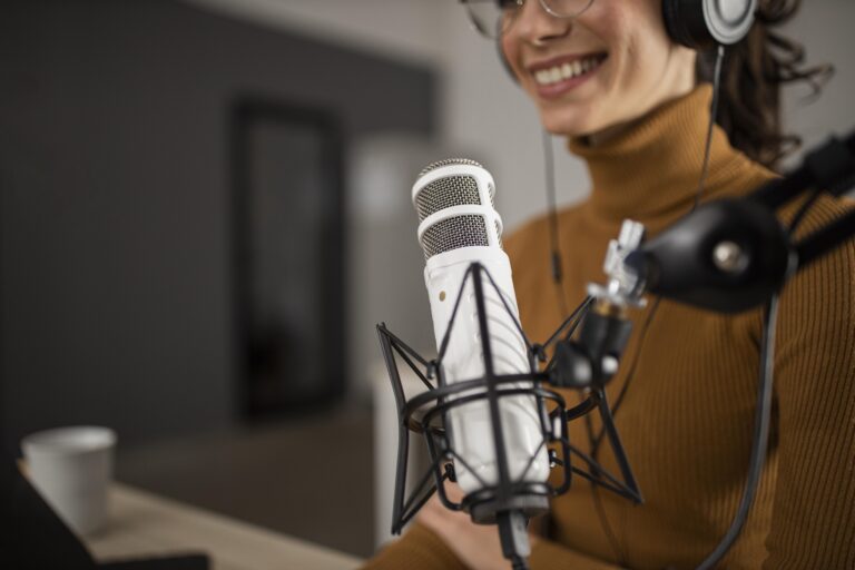A woman in a studio smiles in front of a microphone on a desk.