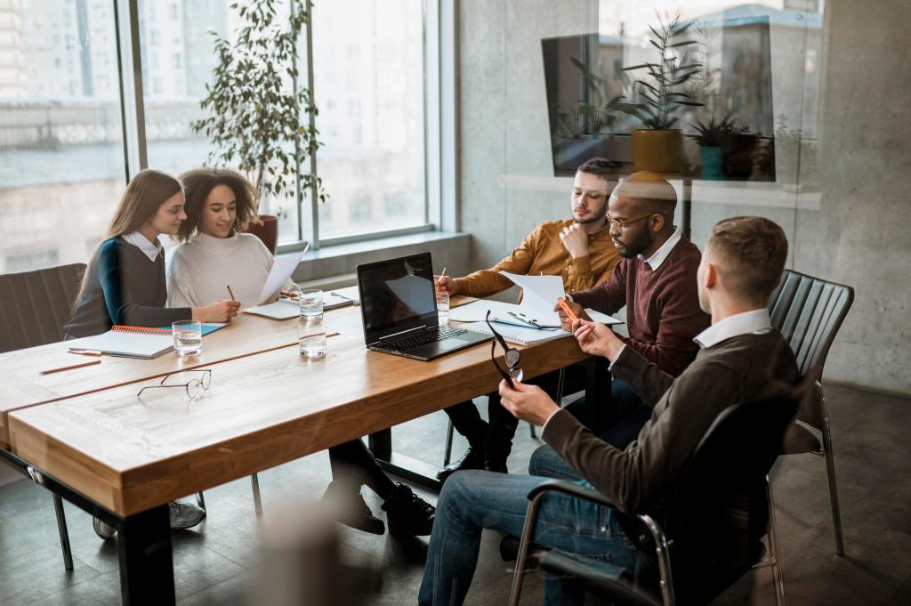 A group of colleagues meet in an office around a conference room table.