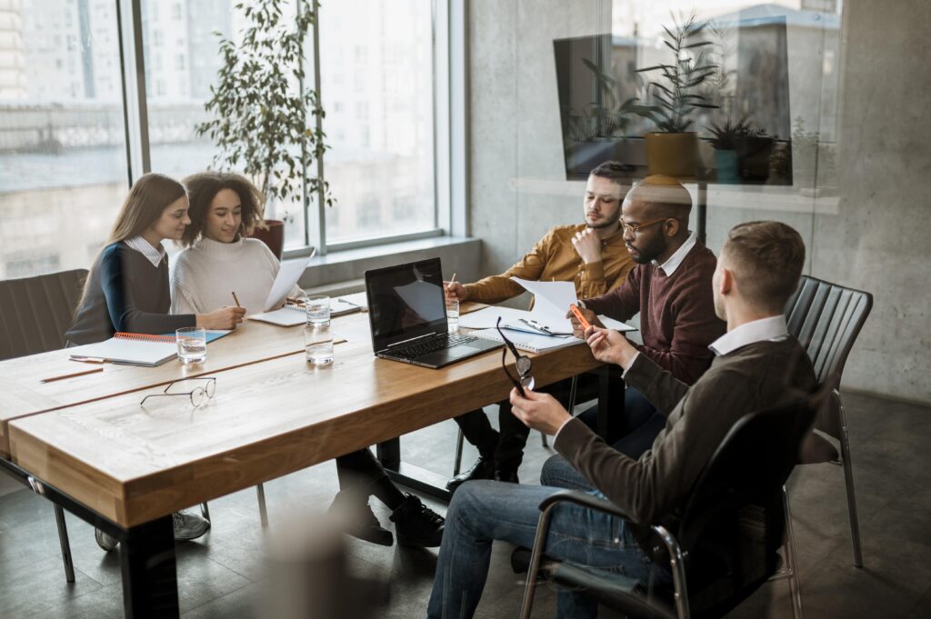 A group of colleagues meet in an office around a conference room table.