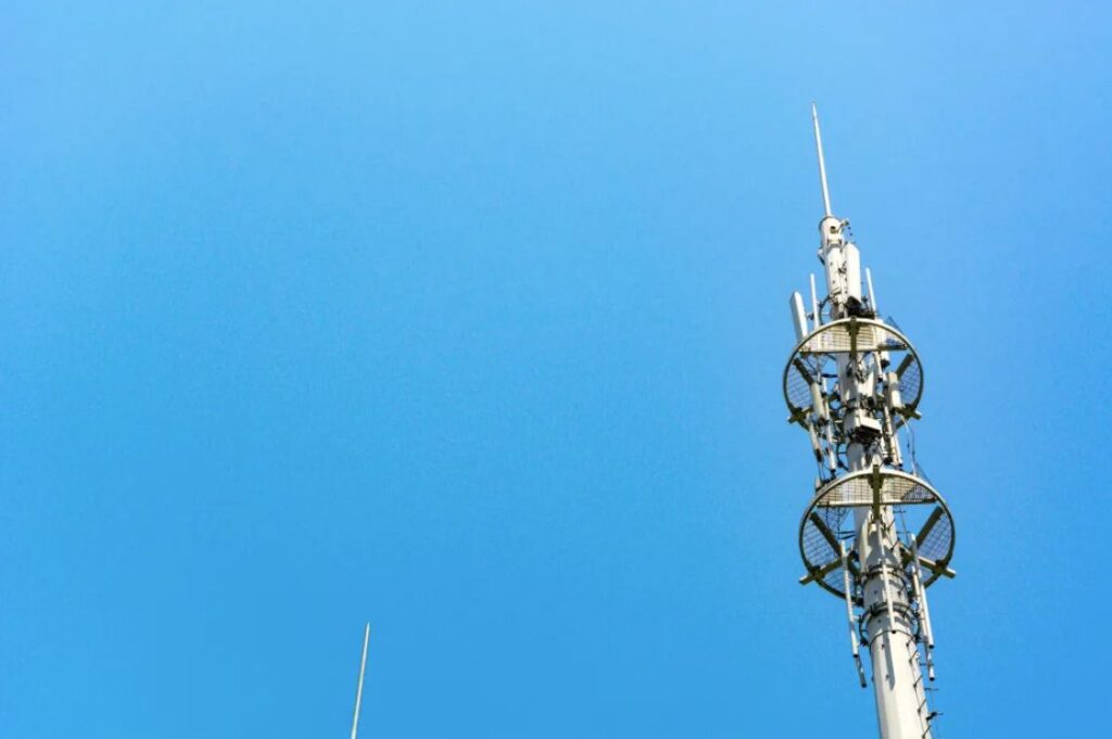 A communications tower shows antennae against a blue sky backdrop.