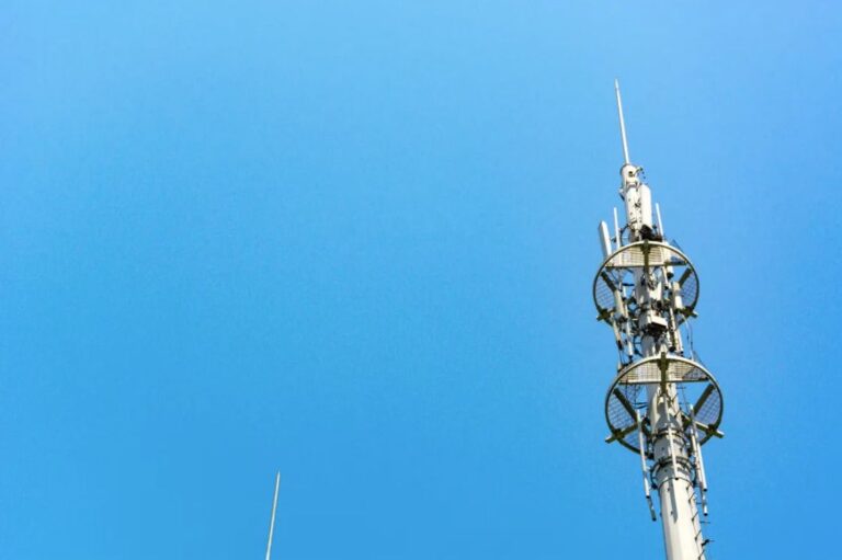 A communications tower shows antennae against a blue sky backdrop.