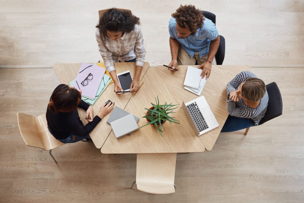 A group of colleagues is shown sitting at a table in an office from above.
