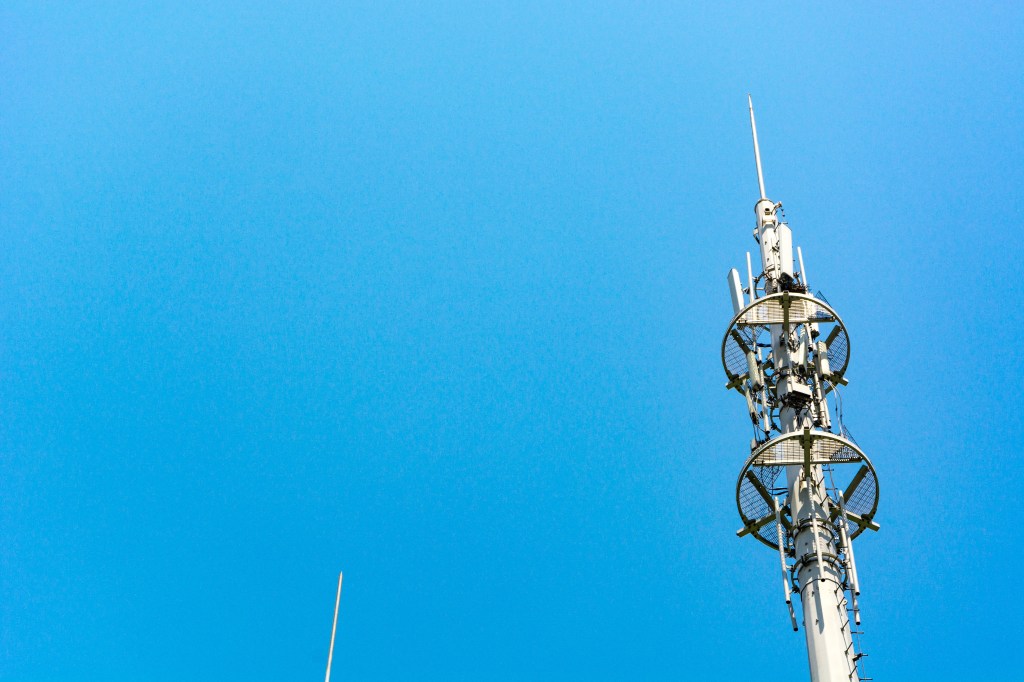 A communications tower shows antennae against a blue sky backdrop.