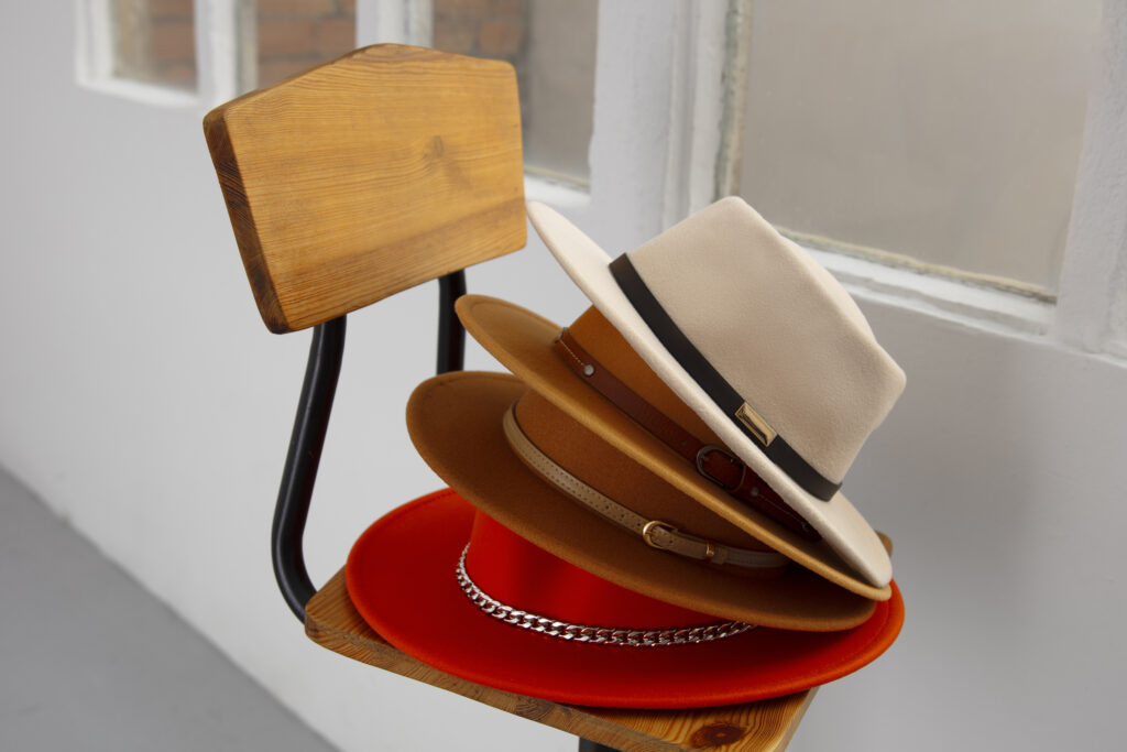 A pile of hats sits stacked on a wooden chair.