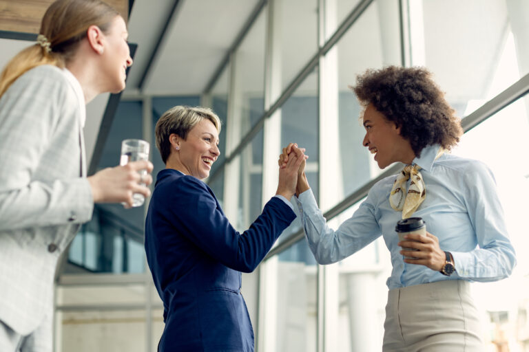 Businesspeople congratulate a young Black woman in an office hallway and give her a high five.