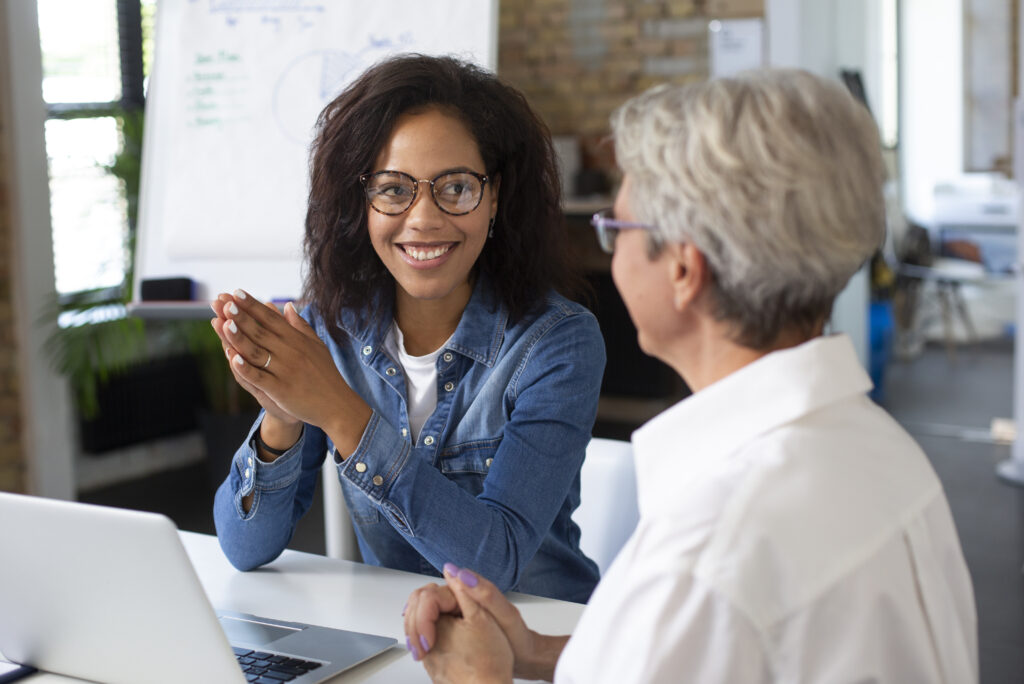 A young Black woman and an older white woman meet at an office table.