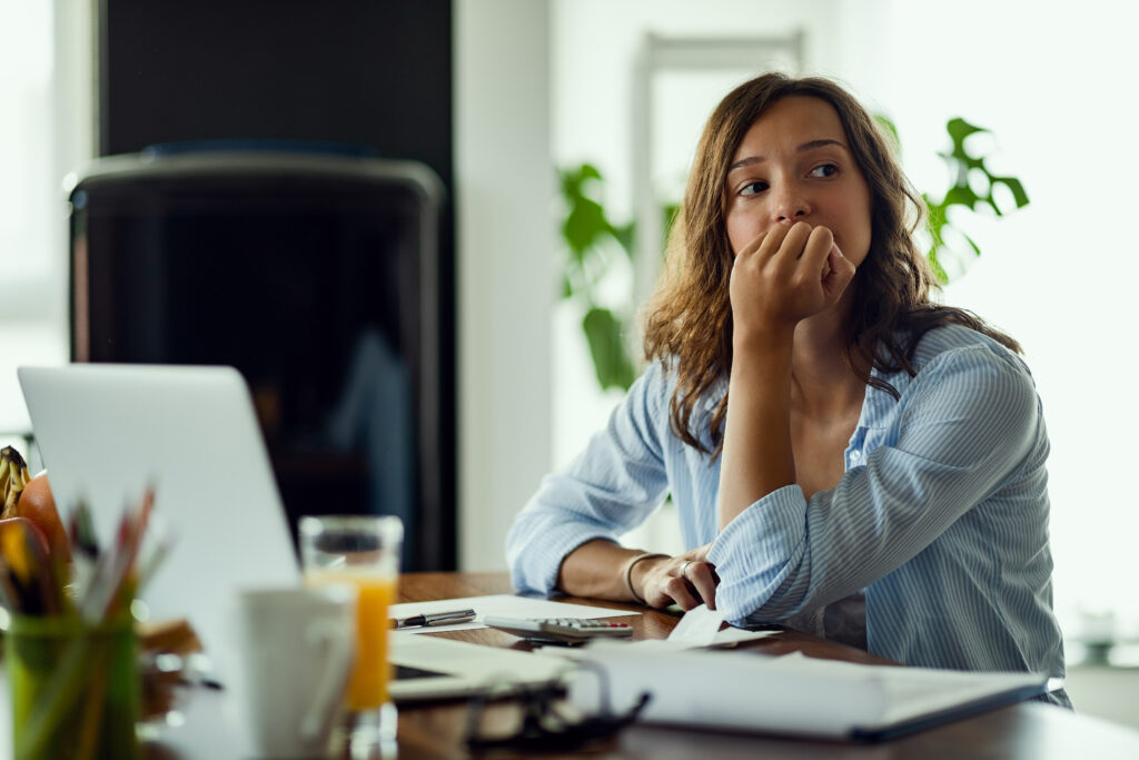 A young woman looks worried at her desk with her left hand scrunched up at her mouth.