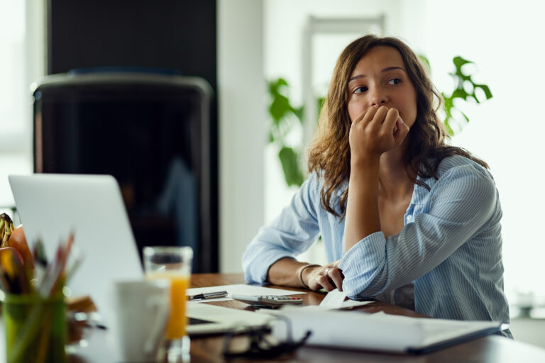 A young woman looks worried at her desk with her left hand scrunched up at her mouth.